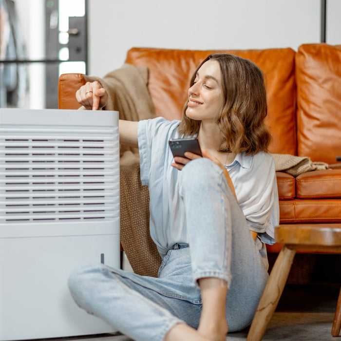 Woman sitting next to an air purifier in her family room and turning it on