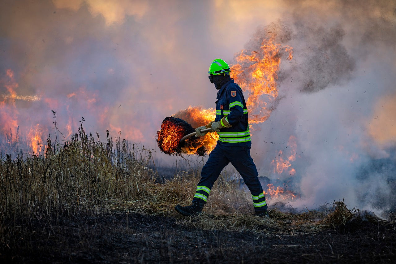 "Firefighter in protective gear carrying a burning log during wildfire containment efforts, with dense smoke in the background.