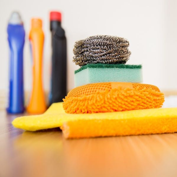 Assorted cleaning supplies on a wooden surface, indicating common household chemicals that an air purifier for chemicals can help reduce.