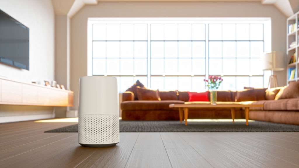 Compact white air purifier on a dark floor in a sunny living room, depicting air purifier benefits with a couch and window in the background