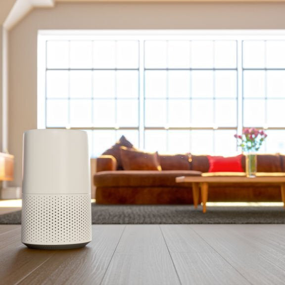Compact white air purifier on a dark floor in a sunny living room, depicting air purifier benefits with a couch and window in the background