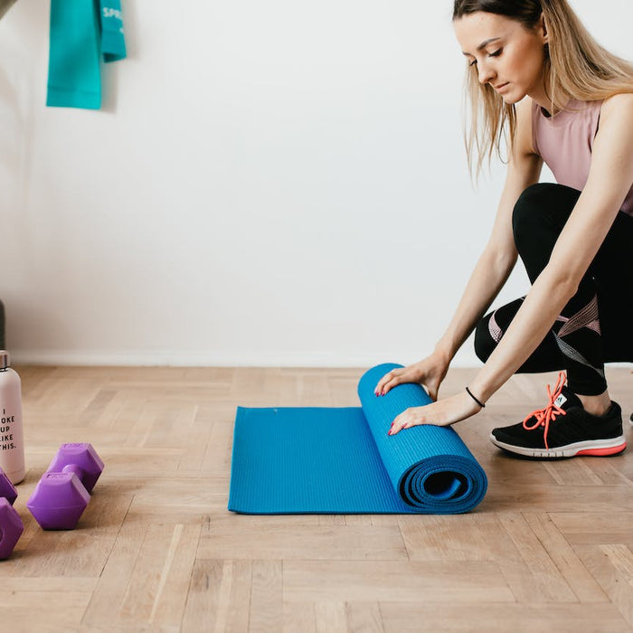 Woman unrolling a blue yoga mat in a well-ventilated home gym space with a portable air purifier, dumbbells, and a water bottle, promoting a clean and healthy exercise environment.
