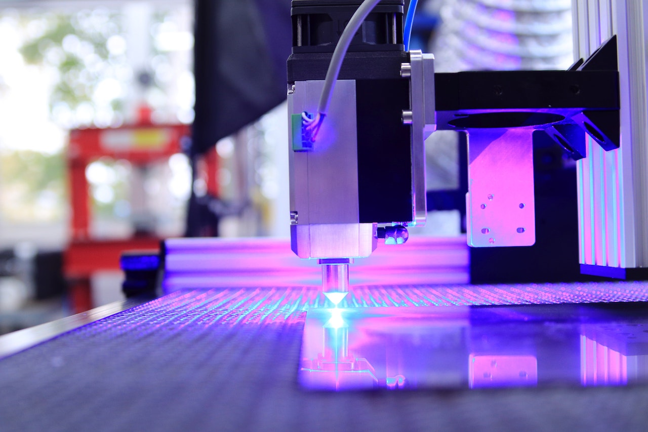 Laser cutter in operation with a blue-violet beam, indicative of the need for a laser cutter air purifier to maintain a safe work environment.